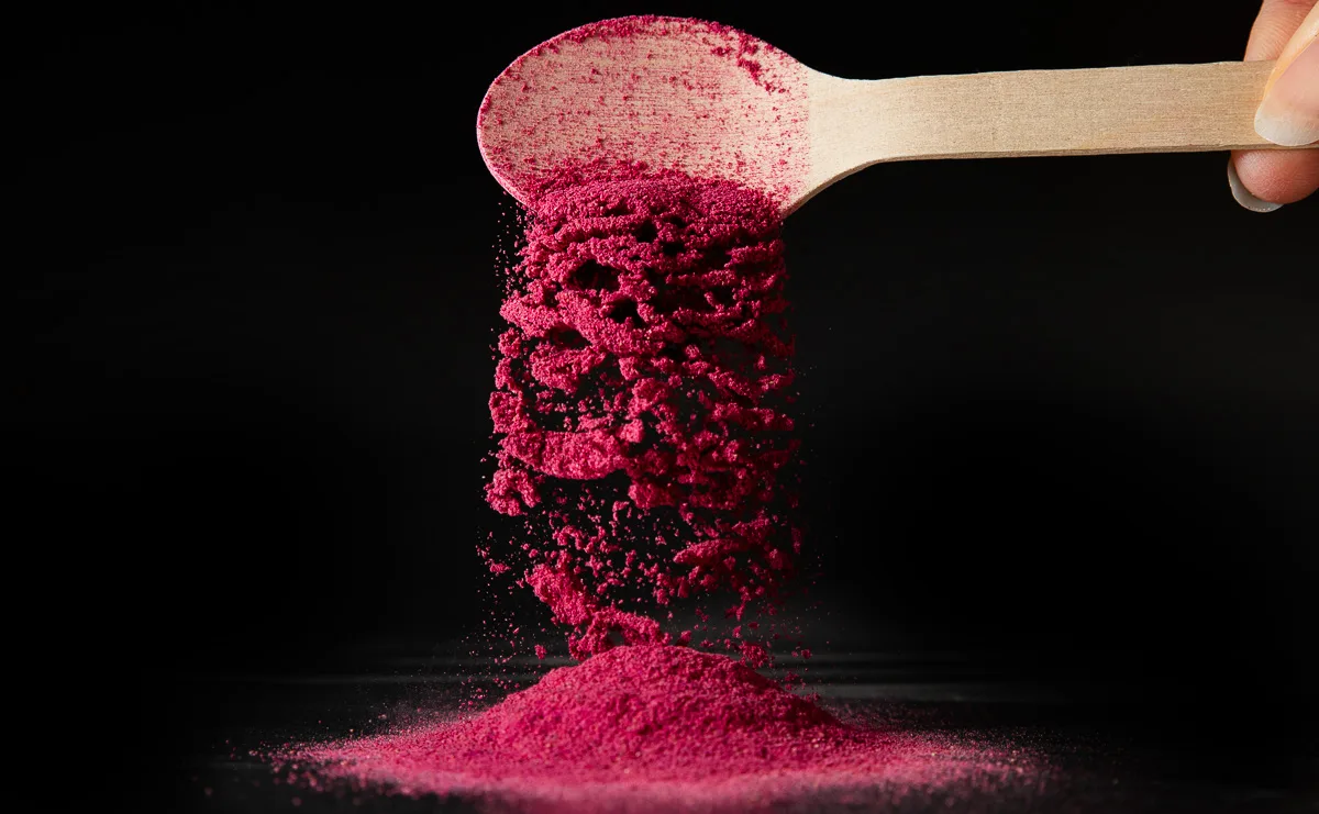Pulver in rosa Pitaya fließt von einem Holzlöffel herunter mit schwarzem Hintergrund.